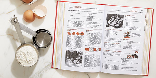 Interior view of Betty Crocker's Picture Cook Book next to a cracked egg and measuring cups