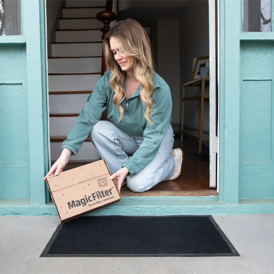 Woman outside of her front door bending down to pick up a delivery box of air filter subscription