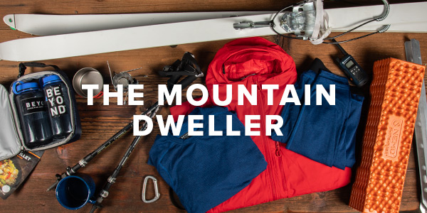 A lay down image of items that a hardened outdoorsman would use on a long excursion in the mountains or other harsh environment. Items include a pair of NATO issued skis, base layers, sleeping pad, insulated jacket, trekking poles and a walkie talkie. Text overlay saying "The Mountain Dweller".