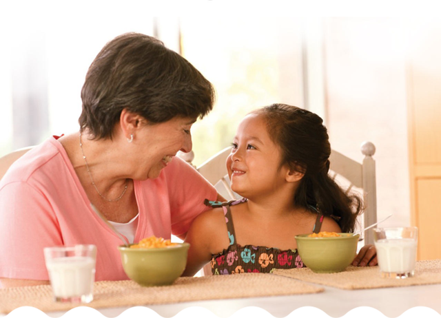 An older woman and a young girl smiling and eating breakfast together.