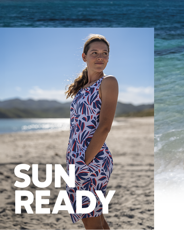 A woman on a sunny beach wearing a sleeveless printed dress.